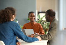 Portrait of young Black businesswoman enjoying work and collaborating on project in meeting with group of colleagues
