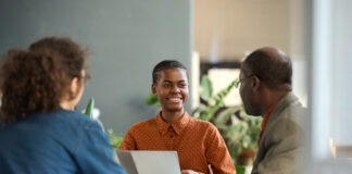 Portrait of young Black businesswoman enjoying work and collaborating on project in meeting with group of colleagues