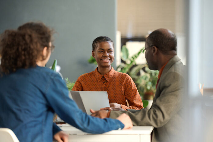 Portrait of young Black businesswoman enjoying work and collaborating on project in meeting with group of colleagues