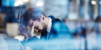 Tired employee holding his head in hands and leaning over laptop