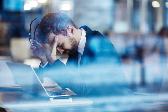 Tired employee holding his head in hands and leaning over laptop