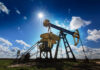 Operating oil and gas well profiled on bright sky with clouds in active European oilfield