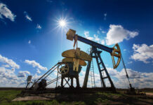 Operating oil and gas well profiled on bright sky with clouds in active European oilfield