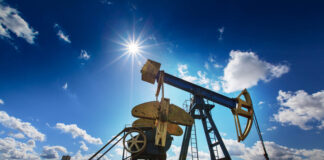 Operating oil and gas well profiled on bright sky with clouds in active European oilfield