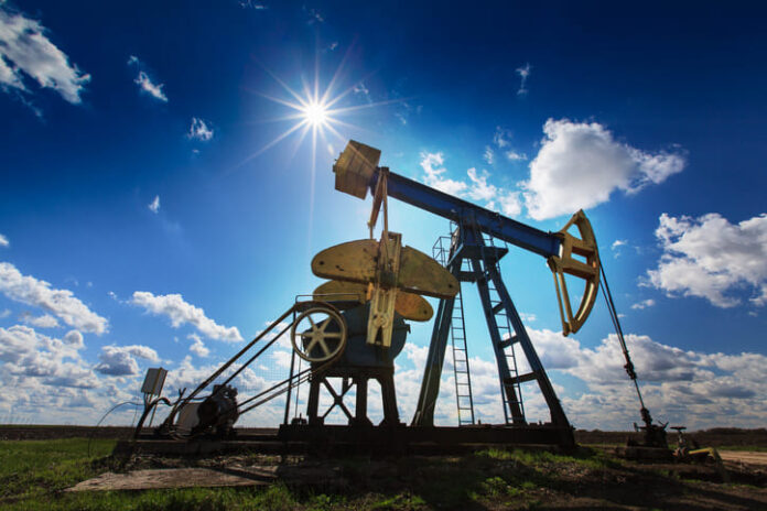 Operating oil and gas well profiled on bright sky with clouds in active European oilfield