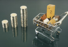 Hand choosing mini wood house from row of coin money with cart on dark table, selective focus, Planning to buy property.