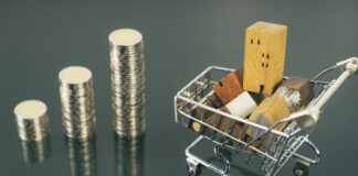 Hand choosing mini wood house from row of coin money with cart on dark table, selective focus, Planning to buy property.