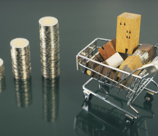Hand choosing mini wood house from row of coin money with cart on dark table, selective focus, Planning to buy property.
