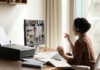 Side view Indian businesswoman in headphones engaged in virtual conference with diverse colleagues, using computer, chatting online by video call, sitting at desk, business partners negotiating