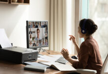 Side view Indian businesswoman in headphones engaged in virtual conference with diverse colleagues, using computer, chatting online by video call, sitting at desk, business partners negotiating