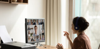 Side view Indian businesswoman in headphones engaged in virtual conference with diverse colleagues, using computer, chatting online by video call, sitting at desk, business partners negotiating