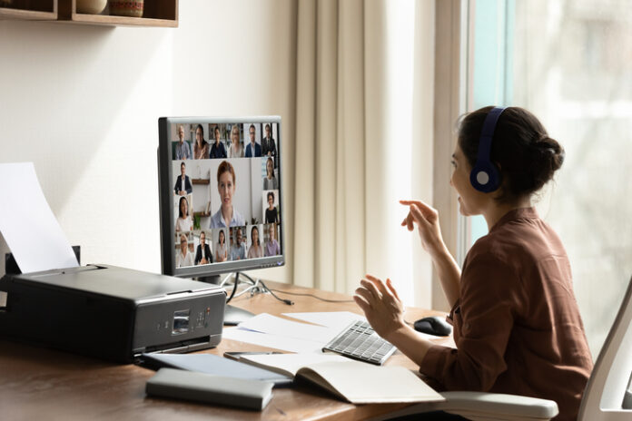 Side view Indian businesswoman in headphones engaged in virtual conference with diverse colleagues, using computer, chatting online by video call, sitting at desk, business partners negotiating