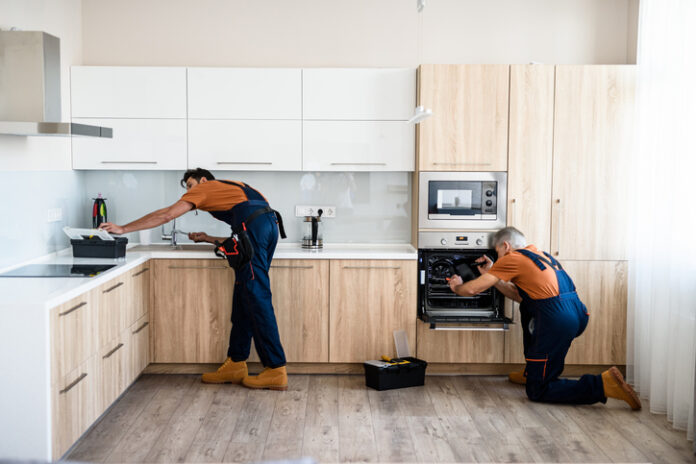 Repair. Two handymen, workers in uniform fixing, installing furniture and equipment in the kitchen, using screwdriver indoors. Furniture repair and assembly concept Two handymen, workers in uniform fixing, installing furniture and equipment in the kitchen, using screwdriver indoors.