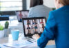 Back view of two business women speaking on video call with diverse colleagues on online briefing with laptop in the office.