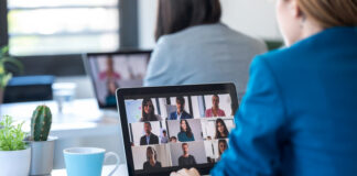 Back view of two business women speaking on video call with diverse colleagues on online briefing with laptop in the office.