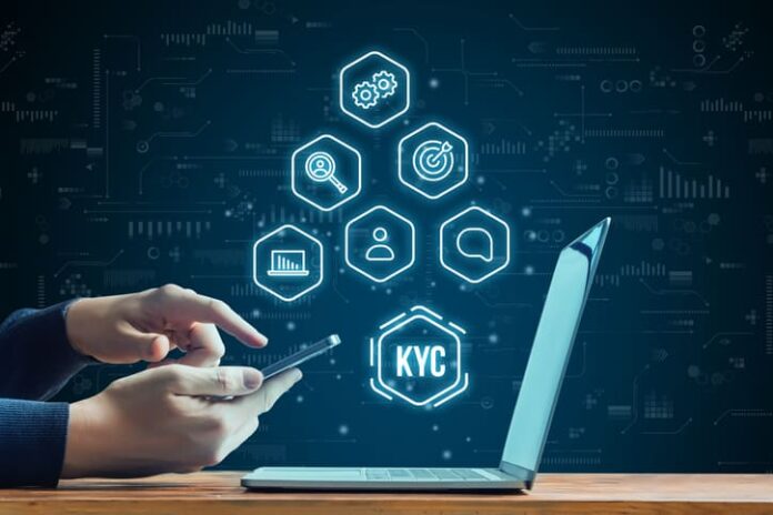 Hand with smartphone next to laptop. KYC concept