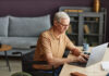 Senior man with disability sitting on wheelchair and typing on laptop