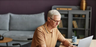 Senior man with disability sitting on wheelchair and typing on laptop