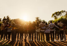 Back view of happy multigenerational people having fun in a public park during sunset time - Community and support