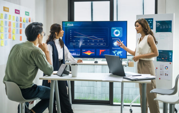 iStock-2168414563 (1) worman leader presenting a financial data and strategies in a modern office with charts and graphs displayed on a large screen