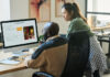 Employees looking at screen of desktop computer while using AI image generator and creating new content by workplace