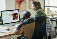 Employees looking at screen of desktop computer while using AI image generator and creating new content by workplace