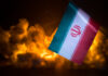USA and Iran small flags on burning dark background. Concept of crisis of war and political conflicts between nations.