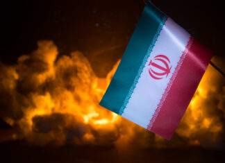 USA and Iran small flags on burning dark background. Concept of crisis of war and political conflicts between nations.