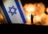 Israel small flag on burning dark background.