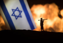 Israel small flag on burning dark background.