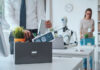 Dismissed business people packing their belongings and leaving the office, a robot is sitting at the desk and working: the impact of AI on jobs
