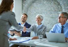 Happy member of human resource team shaking hands with female candidate on job interview in the office.