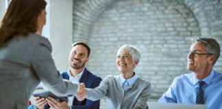 Happy member of human resource team shaking hands with female candidate on job interview in the office.