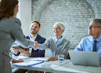 Happy member of human resource team shaking hands with female candidate on job interview in the office.