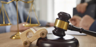 Toy car, sound block, gavel and scales of justice on table, with accident Attorneys in background