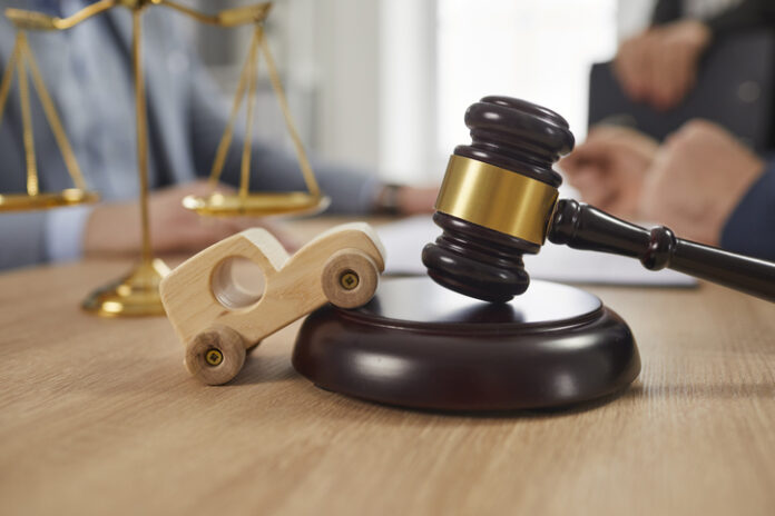 Toy car, sound block, gavel and scales of justice on table, with accident Attorneys in background