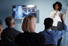 Back view of Black male business meeting attendee raising hand to ask question to colleague during presentation on latest updates in AI technologies