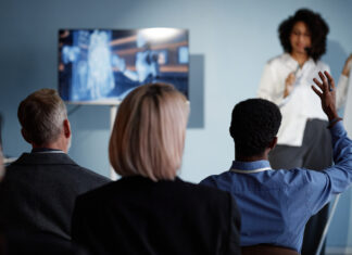 Back view of Black male business meeting attendee raising hand to ask question to colleague during presentation on latest updates in AI technologies