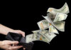 Hundred American dollars banknotes flying out of a leather wallet in male hands