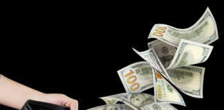 Hundred American dollars banknotes flying out of a leather wallet in male hands