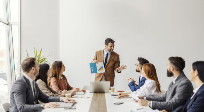 An executive standing and showing visual chart with financial report to his team of experts at boardroom.