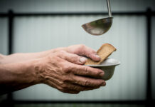 The man in the hands holding a plate and a piece of bread.