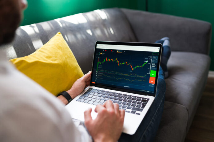 trading-finances-young-man-resting-couch-while-checking-stock-market-laptop (1) (1) Man checking trading on laptop