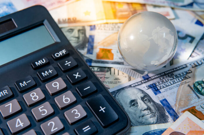 iStock-1056322826 (1) Global business and economy. World globe crystal glass and calculator on various international money banknotes.