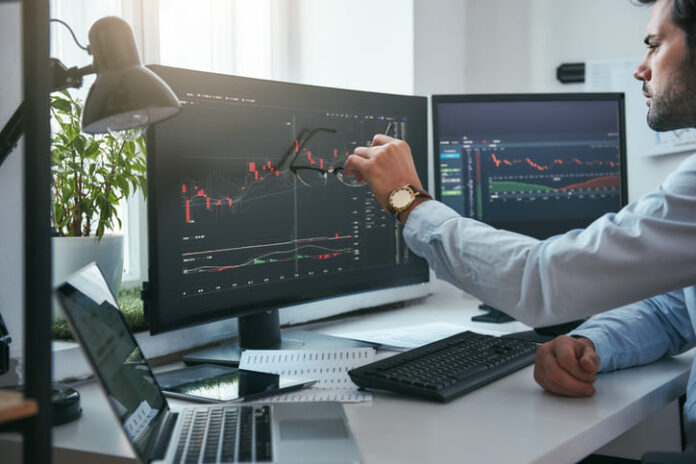 iStock-1147352139 (1) Young trader is pointing at graphs on computer screen and analyzing data while working in his modern office.
