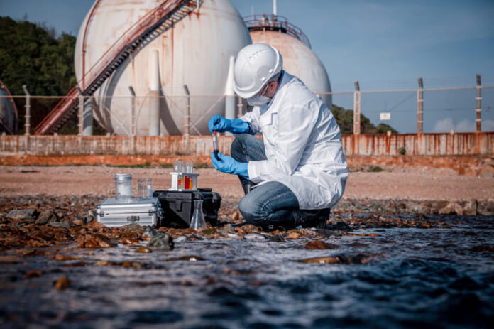 iStock-1396964668 (1) Scientist wearing safety uniform and glove under working water analysis and water quality by get waste water to check case in laboratory is environment pollution problem
