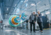 Factory Digitalization: Two Industrial Engineers Use Tablet Computer, Analysing Data about a 3D Model of Green Energy Engine. Industry 4 High-Tech Electronics Facility with Manufacturing Products