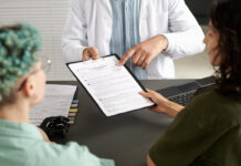 Rear view of couple of girls signing medical contract during meeting with doctor in office