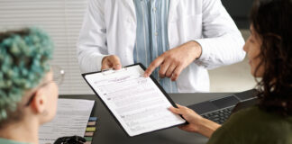 Rear view of couple of girls signing medical contract during meeting with doctor in office