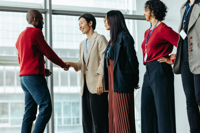 iStock-2163291735 (1) Successful team introduction during a corporate meeting. Diverse professionals engaging in a positive interaction, fostering a collaborative office environment.